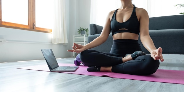 Primo piano della donna della mano che fa esercizi di yoga del loto sul tappetino yoga con formazione online sul tablet a casa mattina concetto di relax e meditazione