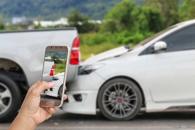Закройте руку женщины, держащей смартфон и фотографировать автомобиль аварии