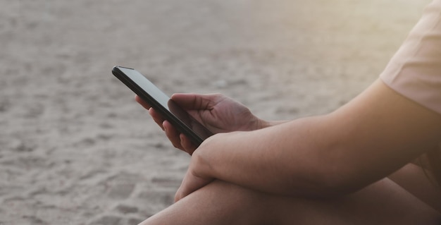 Close up of the hand of a woman playing mobile phone by the sea
at sunset