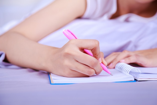 close up hand of woman writing a book on her bed