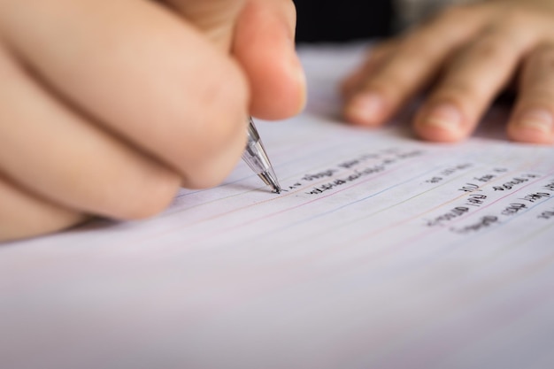 close-up of hand writing on book using pen