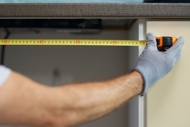 Close up of hand of young repairman professional plumber using measure tape while doing plumbing