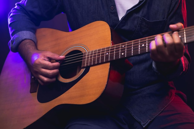 Close-up handen jonge man akoestische gitaar spelen op het podium live in concert. Met neonlicht. Jonge man beoefenen van muziek en solo gitaar op de show.