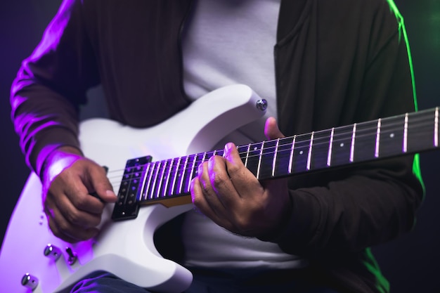 Close-up handen jonge man rocker elektrische gitaar spelen op het podium live in concert. Met neonlicht. Jonge man beoefenen van heavy metal muziek en solo gitaar op de show.