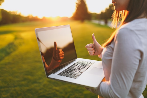 Close-up handen op toetsenbord. Vrouw die op laptop pc-computer werkt met een leeg zwart leeg scherm om ruimte in het park op groen graszonnegras buitenshuis te kopiëren. Mobiel kantoor. Freelance bedrijfsconcept.