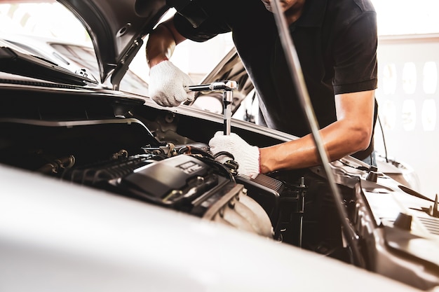 Close-up handen van automonteur gebruiken de moersleutel om de motor van een auto in auto auto garage te repareren