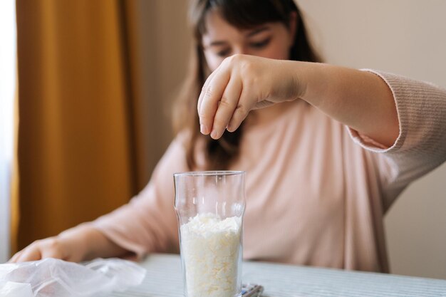 Close-up handen van gefocuste vrouwelijke ambachtslieden die droog mengsel of sojawas op glas gieten om kaarsen te maken