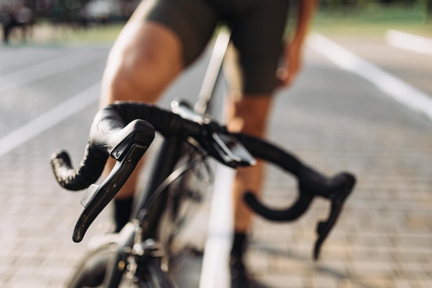 검은색 스포츠 자전거 핸들 바를 닫습니다 신선한 공기에서 훈련 후 휴식을 취하는 백인 자전거 타는 사람의 배경을 흐리게 합니다. 건강하고 활동적인 생활 방식의 개념