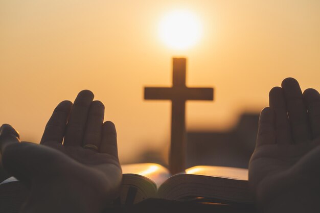 Photo close-up of hands against cross during sunset