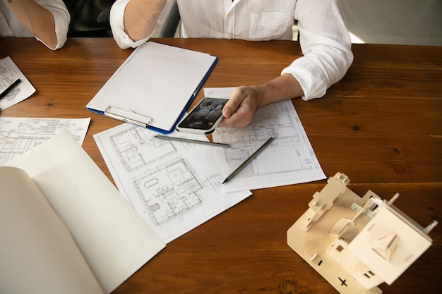 Close up hands of architect-engineer and young couple during presentation of future house. Top view table with documents, blueprint. First home, industrial, building concept. Moving to new live place.