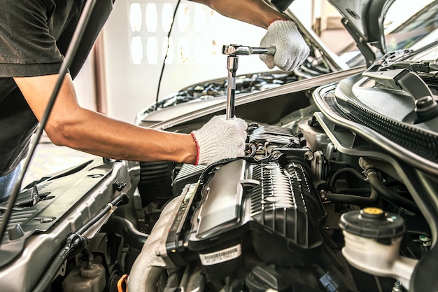 Mani del primo piano del meccanico automatico utilizzando la chiave per la manutenzione del motore dell'auto.