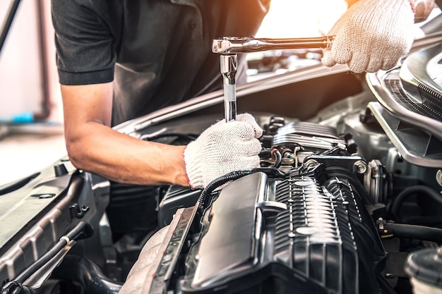 Foto mani ravvicinate di un meccanico che utilizza la chiave per la manutenzione del motore dell'auto.