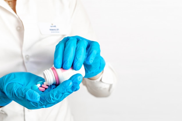 Close-up of hands in blue medical gloves holding a bottle with pills. The doctor gives a medication, vitamins and antibiotics to treat health in the palm of hand on light background with copy space.