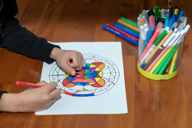 Close up hands of boy painting a mandala with his colored markers