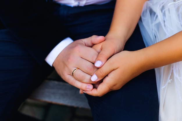 Foto primo piano delle mani della sposa e dello sposo che si siedono sulla panchina