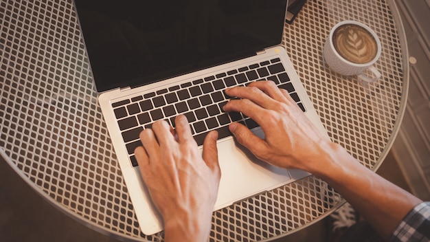Chiudere le mani dell'uomo d'affari che utilizza il computer portatile con una tazza di caffè sul tavolo, vista dall'alto.