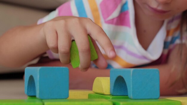 Foto le mani vicine della bambina concentrata a casa giocano con blocchi di legno colorati su flor.