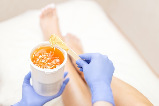 Close-up hands of cosmetologist in blue gloves holding paste for sugaring depilation 