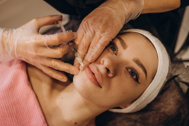 Close up of hands of cosmetologist making botox injection in female lips She is holding syringe The young beautiful woman is receiving procedure with enjoyment