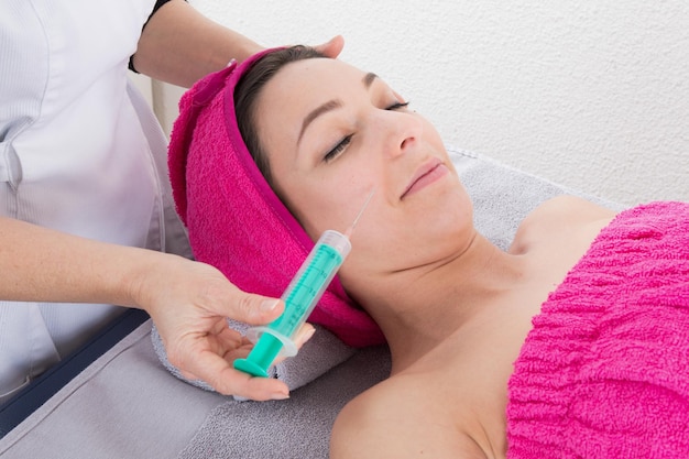 Close up of hands of cosmetologist making botox injection in female lips. She is holding syringe.