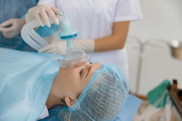 Photo close up hands of doctor anesthesiologist holding breathing mask on patient face during operation