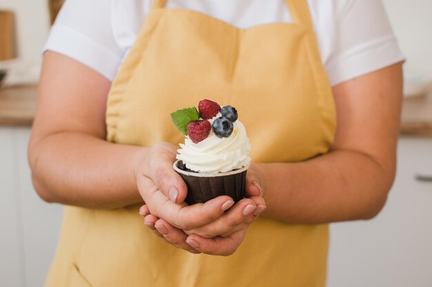 マフィンまたは野生のベリーで飾られたカップケーキと白いガウンの女性のパティシエの手のクローズアップ