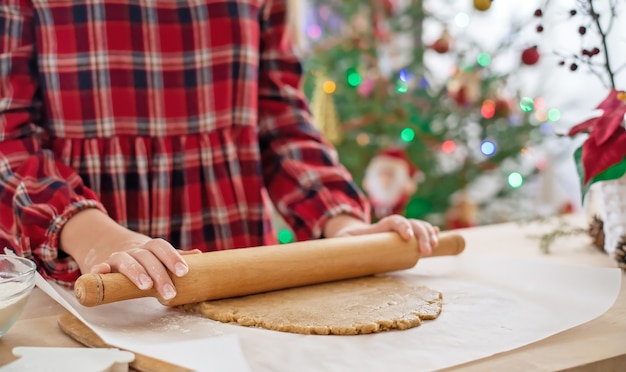 ジンジャーブレッドクッキーの生地を広げる女の子のクローズアップの手。クリスマスのベーキング。