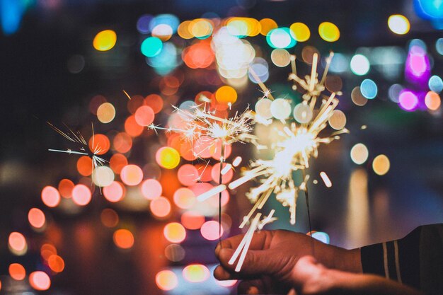 Photo close-up of hands holding illuminated sparkler at night