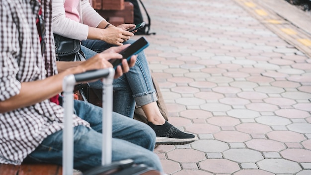 Close up hands holding mobile of couple with bags waiting for the train.