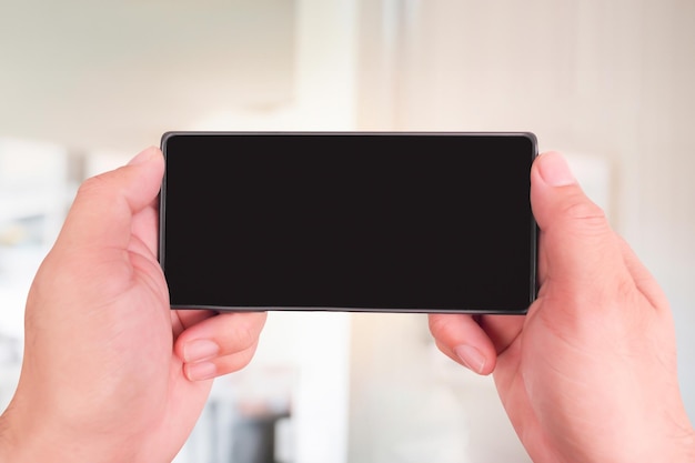 Close up of hands holding smartphone with blank screen over blurred background