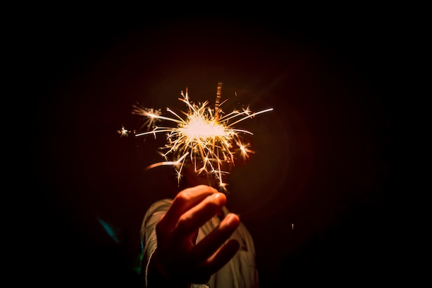 Chiuda su delle mani che tengono le stelle filante alla notte, fuoco d'artificio celebrano alla notte