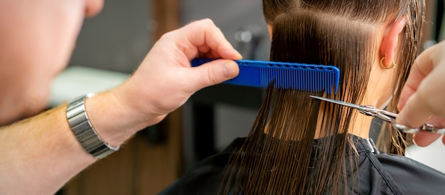 Photo close up of hands of male hairdresser cutting long hair of young woman holding scissors