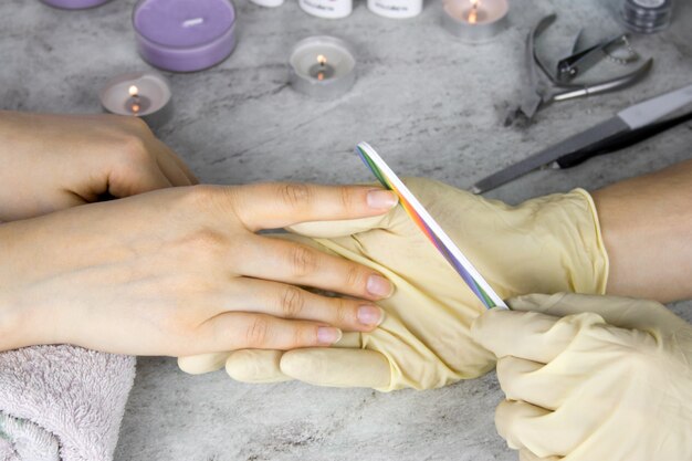 Foto chiuda sulle mani del manicure in guanti con la lima per unghie