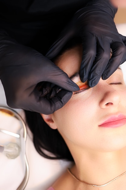 Close-up of the hands of the master of lamination of cilia, the master performs the procedure by gluing the roller for curling eyelashes to the client's eyelid