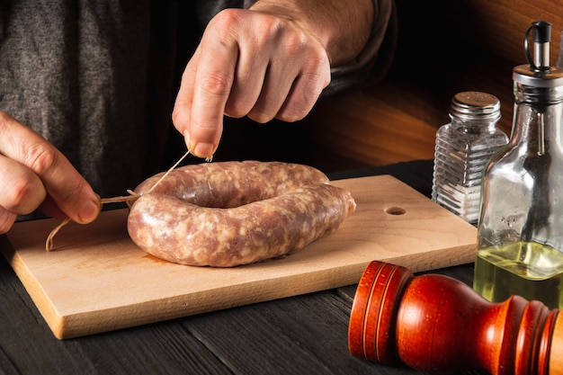 自家製ソーセージの糸を結ぶ料理人のクローズアップの手。まな板の上で肉とスパイスでソーセージを調理する