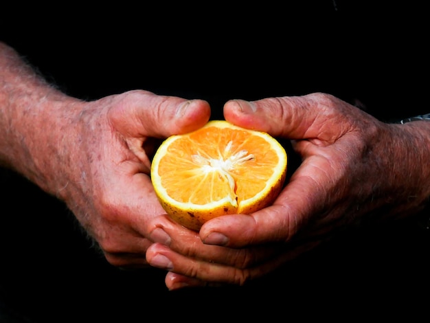 Photo close-up of hands of an old man holding a half of a yellow lemon