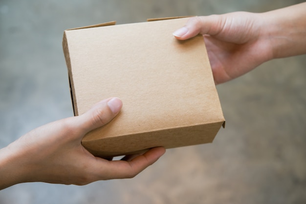 Photo close up hands passing and receiving small brown box package.