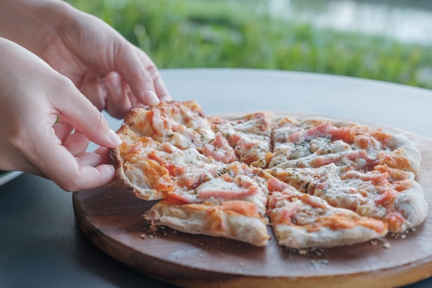 Close up hands pick up pizza in wooden tray.