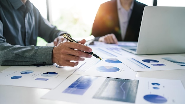 Close up hands pointing chart and graph of businessman and businesswoman using laptop and discussing at meeting