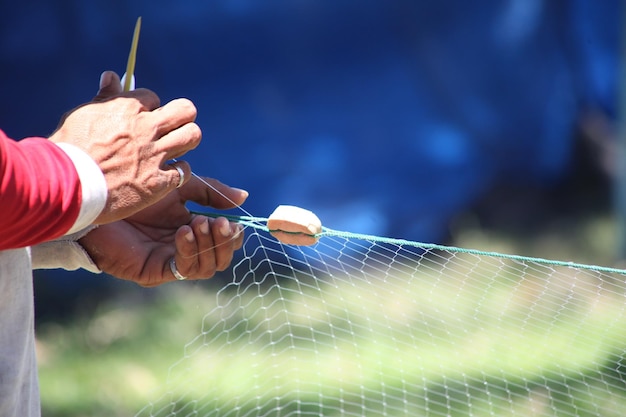 Photo close-up of hands repairing fishing net