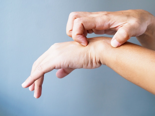 Close-Up of hands scratching on arms from itching of skin diseases, isolated on gray wall