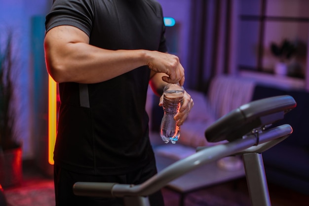 Close up of hands of sports man drinking opening water bottle doing fitness exercise