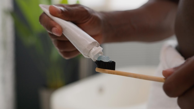 Близкие руки выжимают белую зубную пасту из трубки на зубной щетке утренняя процедура стоматологии