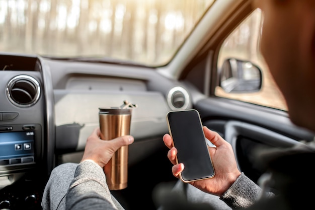 Primo piano delle mani e del termos con lo smartphone in automobile. concetto di viaggio