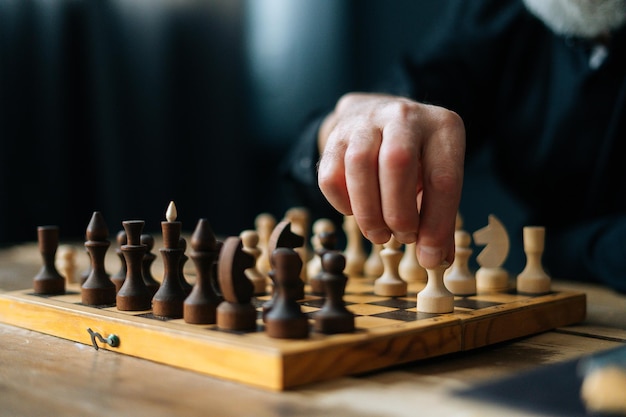 Close-up hands of unrecognizable bearded chess player performing move with pawn piece on wooden chessboard, selective focus. Closeup of board chess game execution of move by player grandmaster