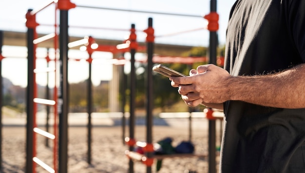 屋外の体操トレーニング中に、バーベルパークで彼のスマートフォンを使用して手のクローズアップ。