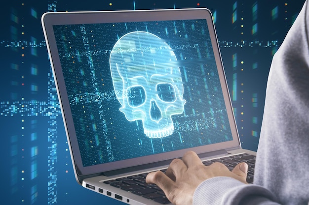 Close up of hands using laptop with glowing digital blue glitch skull on screen Blurry background Virus crime and hacking concept