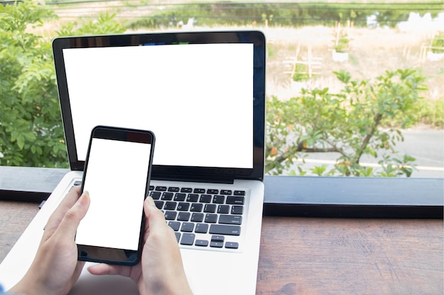 close-up of hands using mobile phone over laptop