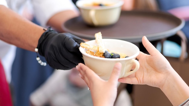 close up of the hands of a waiter giving dessert to a customer. cup of fruit in the hands.