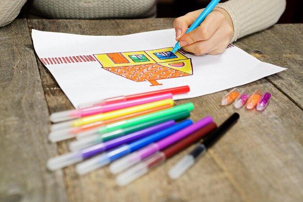 Close up of the hands of woman drawing a house with color pencils